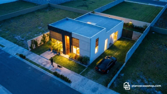 Vista aérea nocturna de casa pequeña Mía planos 1 piso con fachada moderna en concreto, madera y ventanales iluminados.
