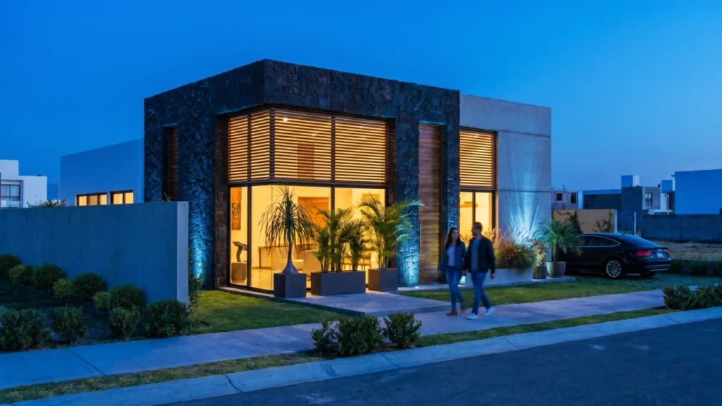 Fachada moderna de casa pequeña Mía planos 1 piso con piedra negra, concreto y ventanales iluminados al atardecer.