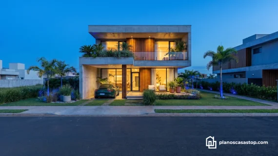 Fachada de hormigón y madera bajo los planos de casa moderna ca86 con iluminación cálida y jardines.