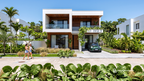 Fachada de dos niveles con madera y blanco basada en los planos de casa moderna arrayán rodeada de vegetación tropical.