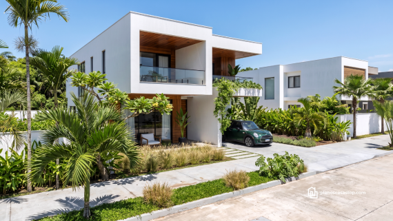 Fachada minimalista en blanco y madera integrada a los planos de casa moderna arrayán con vegetación tropical.