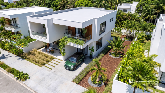 Fachada minimalista blanca con vegetación tropical basada en los planos de casa moderna arrayán y acabados en madera.