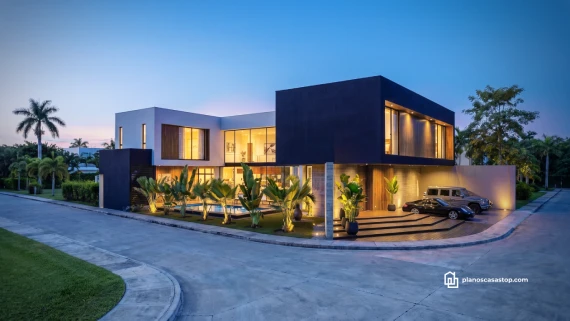 Fachada iluminada de los planos de casa moderna Olmo con volúmenes negros, piscina y vegetación tropical al atardecer.